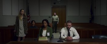 Movie still from “Palmer” (2021), directed by Fisher Stevens – A man and a woman sitting at a table in a courtroom; Wide shot, Low angle