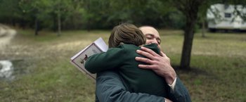 Movie still from “Palmer” (2021), directed by Fisher Stevens – A man and a child hug in a field; Close Up shot, Over the shoulder angle