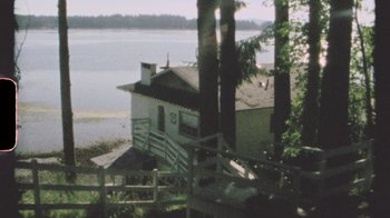 Movie still from “Pamela: A Love Story” (2023), directed by Ryan White – A house sitting next to a body of water; Extreme Wide shot, High angle
