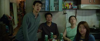 Movie still from “Parasite” (2019), directed by Bong Joon Ho – A group of people sitting around a table with drinks; Medium shot, Over the shoulder angle