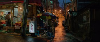 Movie still from “Parasite” (2019), directed by Bong Joon Ho – A person standing under an umbrella on a rainy street; Extreme Wide shot, High angle