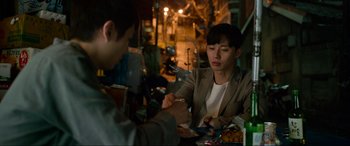 Movie still from “Parasite” (2019), directed by Bong Joon Ho – Two people are sitting at a table eating food; Medium shot, Over the shoulder angle