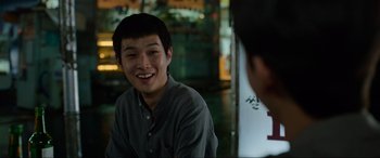Movie still from “Parasite” (2019), directed by Bong Joon Ho – A young man smiling while sitting in front of a mirror; Close Up shot, Over the shoulder angle