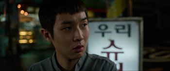 Movie still from “Parasite” (2019), directed by Bong Joon Ho – A young asian man looking at the camera; Close Up shot, Over the shoulder angle