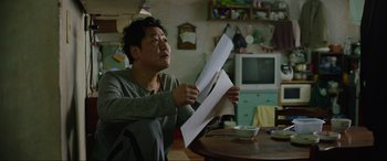 Movie still from “Parasite” (2019), directed by Bong Joon Ho – A man holding a piece of paper in his hands; Medium shot, Low angle