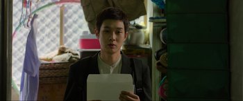 Movie still from “Parasite” (2019), directed by Bong Joon Ho – A man holding a piece of paper in a cluttered room; Close Up shot, Over the shoulder angle