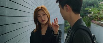 Movie still from “Parasite” (2019), directed by Bong Joon Ho – A young woman and a young man standing next to each other in front of a brick wall; Medium shot, Over the shoulder angle