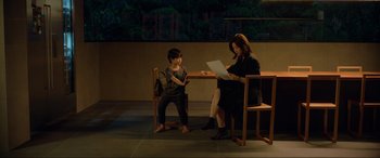 Movie still from “Parasite” (2019), directed by Bong Joon Ho – A woman sitting at a table with a young boy; Wide shot, High angle