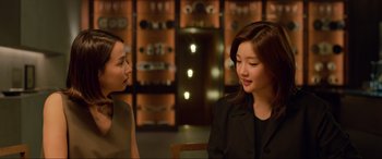 Movie still from “Parasite” (2019), directed by Bong Joon Ho – Two young women are talking in a room; Medium shot, Over the shoulder angle
