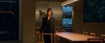 Movie still from “Parasite” (2019), directed by Bong Joon Ho – A woman standing in front of a table in front of a refrigerator; Medium shot, Over the shoulder angle