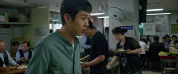 Movie still from “Parasite” (2019), directed by Bong Joon Ho – A group of people standing in a kitchen preparing food; Close Up shot, Over the shoulder angle