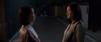 Movie still from “Parasite” (2019), directed by Bong Joon Ho – Two women standing next to each other on the street; Medium shot, Over the shoulder angle