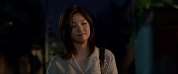 Movie still from “Parasite” (2019), directed by Bong Joon Ho – A young woman with long dark brown hair wearing a white shirt; Close Up shot, Over the shoulder angle