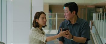 Movie still from “Parasite” (2019), directed by Bong Joon Ho – A man and a woman looking at a cell phone; Medium shot, Over the shoulder angle