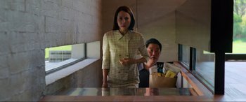 Movie still from “Parasite” (2019), directed by Bong Joon Ho – A woman standing in front of a man eating food; Medium shot, Over the shoulder angle