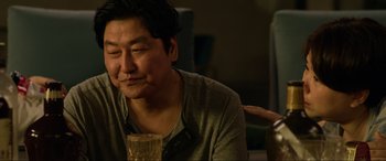 Movie still from “Parasite” (2019), directed by Bong Joon Ho – A man sitting at a table with a drink in front of him; Close Up shot, Over the shoulder angle