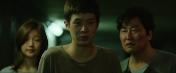 Movie still from “Parasite” (2019), directed by Bong Joon Ho – Two young men standing next to each other in a dark room; Close Up shot, Over the shoulder angle
