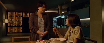 Movie still from “Parasite” (2019), directed by Bong Joon Ho – Two women are sitting at a table with food in front of them; Medium shot, Over the shoulder angle