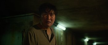 Movie still from “Parasite” (2019), directed by Bong Joon Ho – A man in a gray shirt is in a dark room; Close Up shot, Low angle