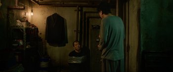Movie still from “Parasite” (2019), directed by Bong Joon Ho – Two men are talking in a dimly - lit room; Medium shot, Over the shoulder angle