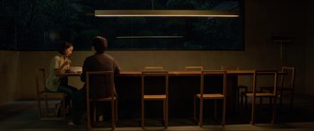 Movie still from “Parasite” (2019), directed by Bong Joon Ho – A person sitting at a table in front of a window; Wide shot, High angle