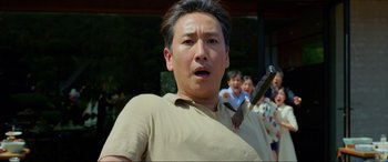 Movie still from “Parasite” (2019), directed by Bong Joon Ho – A man holding a knife in front of a group of people; Medium shot, Low angle