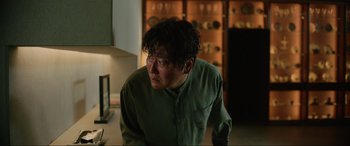 Movie still from “Parasite” (2019), directed by Bong Joon Ho – A man in a green shirt is sitting in front of a stove; Close Up shot, Low angle