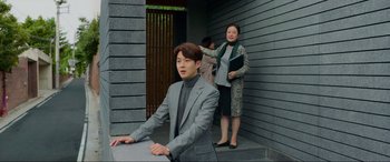 Movie still from “Parasite” (2019), directed by Bong Joon Ho – A man and a woman standing in front of a building; Medium shot, Over the shoulder angle