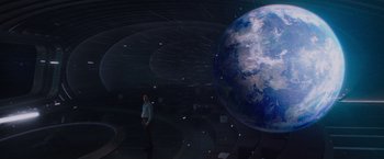 Movie still from “Passengers” (2016), directed by Morten Tyldum – A man standing in front of an image of the earth; Extreme Wide shot, High angle
