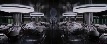 Movie still from “Passengers” (2016), directed by Morten Tyldum – A man standing in a room with a lot of cars; Wide shot, Low angle