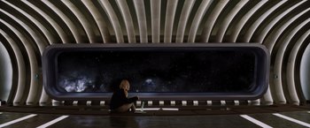 Movie still from “Passengers” (2016), directed by Morten Tyldum – A woman sitting in front of a window with a view of the night sky; Wide shot, Low angle