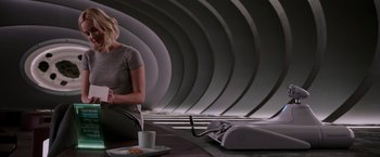 Movie still from “Passengers” (2016), directed by Morten Tyldum – A woman sitting at a table with a cup of coffee; Medium shot, High angle