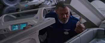 Movie still from “Passengers” (2016), directed by Morten Tyldum – An older man in a uniform looking down at a plane; Close Up shot, High angle