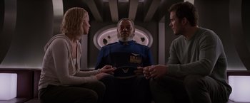 Movie still from “Passengers” (2016), directed by Morten Tyldum – Two men and a woman sitting in front of an older man; Medium shot, Over the shoulder angle