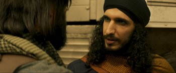 Movie still from “Pathaan” (2023), directed by Siddharth Anand – A man with long hair and a beard is talking to another man; Close Up shot, Over the shoulder angle
