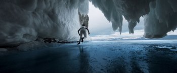 Movie still from “Pathaan” (2023), directed by Siddharth Anand – A man in a white wetsuit riding a surfboard in the ocean; Extreme Wide shot, Low angle
