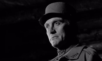 Movie still from “Paths of Glory” (1957), directed by Stanley Kubrick – An old man wearing a top hat in a black and white photo; Close Up shot, Low angle