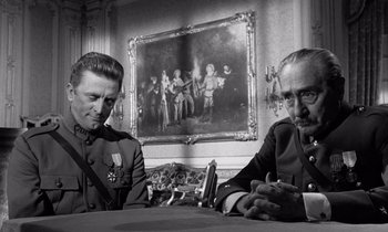 Movie still from “Paths of Glory” (1957), directed by Stanley Kubrick – A black and white photo of two men sitting in front of a painting; Medium shot, Over the shoulder angle