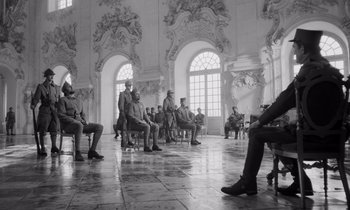 Movie still from “Paths of Glory” (1957), directed by Stanley Kubrick – A black and white photo of men sitting on chairs; Wide shot, Low angle