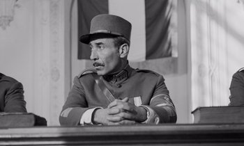 Movie still from “Paths of Glory” (1957), directed by Stanley Kubrick – An old photo of a man in a uniform sitting at a table with a knife in his hand; Medium shot, Low angle