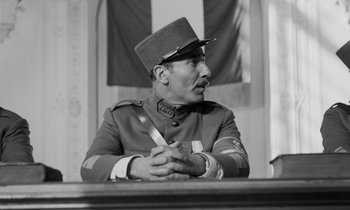 Movie still from “Paths of Glory” (1957), directed by Stanley Kubrick – An old photo of a man in a uniform sitting at a table; Medium shot, Low angle