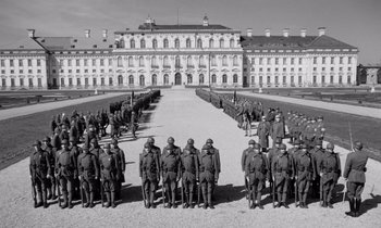 Movie still from “Paths of Glory” (1957), directed by Stanley Kubrick – A black - and - white photo of men in uniform standing in front of a building; Extreme Wide shot, High angle