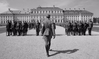 Movie still from “Paths of Glory” (1957), directed by Stanley Kubrick – A black and white photo of a man in a military uniform walking away from a group of soldiers; Wide shot, Low angle