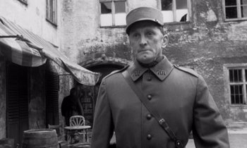 Movie still from “Paths of Glory” (1957), directed by Stanley Kubrick – A man in a uniform standing in front of a building; Medium shot, Low angle