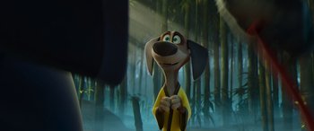 Movie still from “Paws of Fury: The Legend of Hank” (2022), directed by Chris Bailey – A dog with a yellow shirt is standing in front of some trees; Close Up shot, Over the shoulder angle