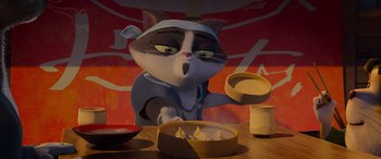 Movie still from “Paws of Fury: The Legend of Hank” (2022), directed by Chris Bailey – A cat is holding a bowl in front of a cake; Close Up shot, Low angle