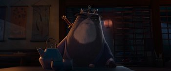 Movie still from “Paws of Fury: The Legend of Hank” (2022), directed by Chris Bailey – A large cat sitting on top of a wooden table; Medium shot, Low angle