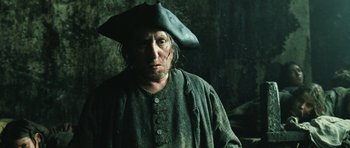 Movie still from “Perfume: The Story of a Murderer” (2006), directed by Tom Tykwer – A man wearing a pirate hat standing next to a wall; Medium shot, Low angle