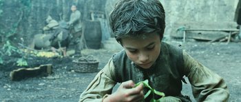 Movie still from “Perfume: The Story of a Murderer” (2006), directed by Tom Tykwer – A young boy holding a piece of food in his hands; Close Up shot, Low angle