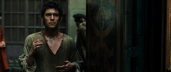 Movie still from “Perfume: The Story of a Murderer” (2006), directed by Tom Tykwer – A man standing in front of a wooden wall; Medium shot, Over the shoulder angle